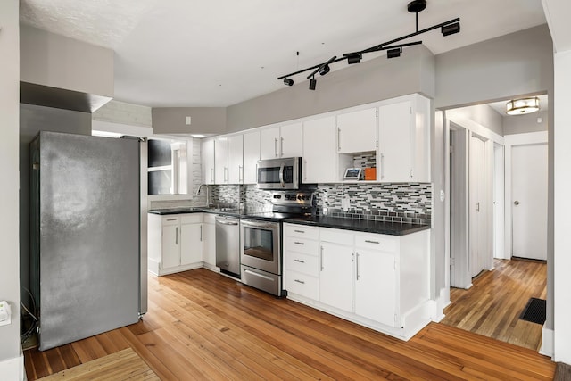 kitchen featuring light wood finished floors, appliances with stainless steel finishes, white cabinetry, dark countertops, and backsplash