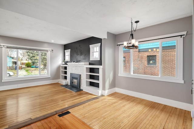 unfurnished living room featuring visible vents, a fireplace with flush hearth, wood-type flooring, baseboards, and a chandelier