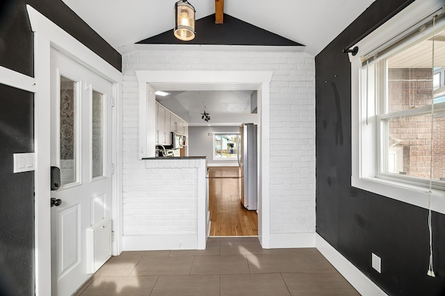 hallway featuring tile patterned flooring, brick wall, vaulted ceiling with beams, and baseboards