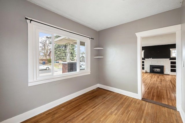 spare room featuring baseboards, a brick fireplace, and hardwood / wood-style floors