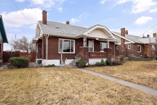 bungalow-style home featuring brick siding, fence, roof with shingles, a front yard, and a chimney