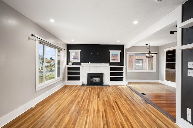 unfurnished living room featuring built in features, baseboards, recessed lighting, a brick fireplace, and light wood-type flooring