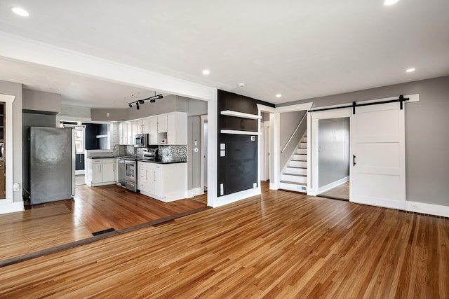 unfurnished living room with recessed lighting, a barn door, and wood finished floors