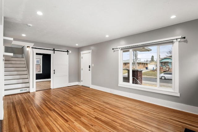 unfurnished living room featuring visible vents, stairway, a barn door, recessed lighting, and wood finished floors