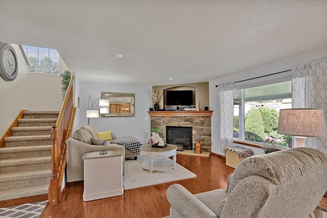 living area with stairway, a stone fireplace, and wood finished floors