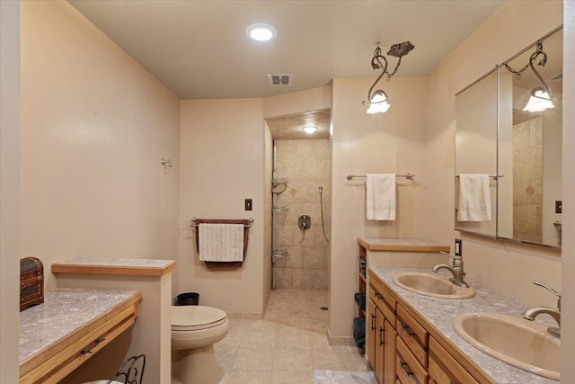 bathroom featuring baseboards, tiled shower, visible vents, and a sink