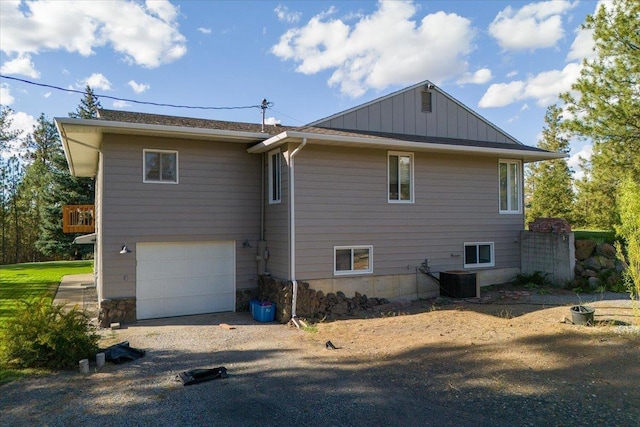 view of side of property with central air condition unit, an attached garage, board and batten siding, and driveway