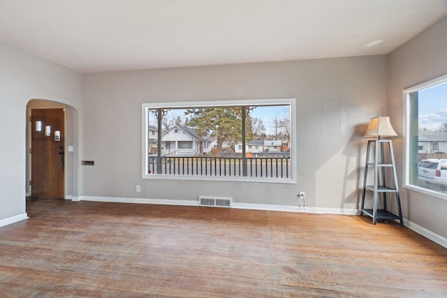 unfurnished room featuring wood finished floors, arched walkways, visible vents, and baseboards