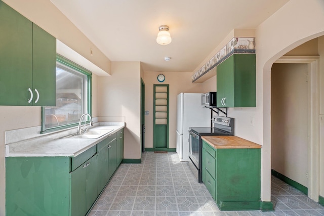 kitchen featuring baseboards, a sink, light countertops, appliances with stainless steel finishes, and green cabinets