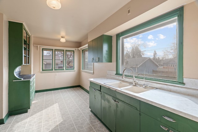 kitchen featuring a sink, baseboards, green cabinets, and light countertops