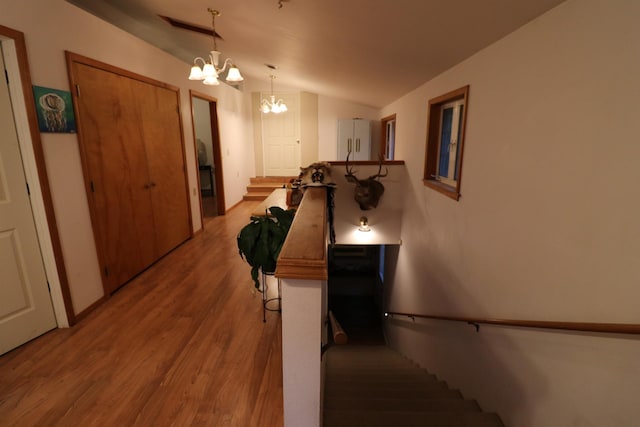 hallway with vaulted ceiling, a notable chandelier, visible vents, and wood finished floors