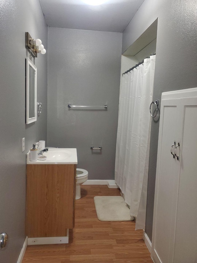 bathroom featuring baseboards, toilet, a shower with curtain, wood finished floors, and vanity