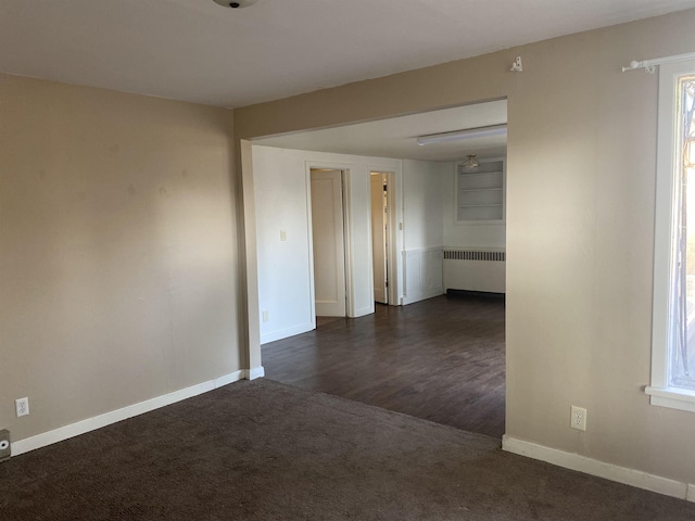 unfurnished room featuring dark colored carpet, baseboards, and radiator heating unit