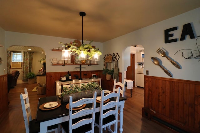 dining room with wooden walls, wood finished floors, arched walkways, and wainscoting