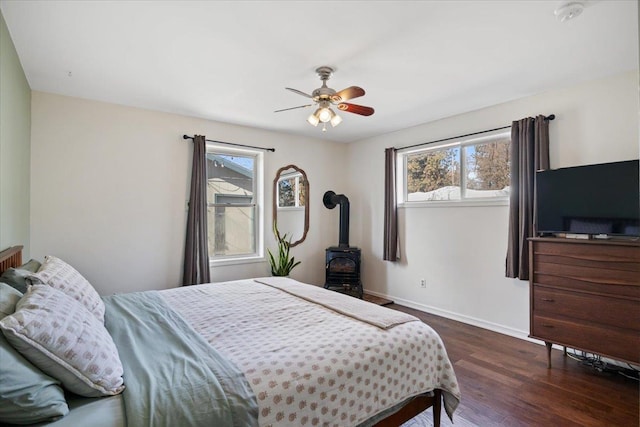 bedroom with dark wood-type flooring, a wood stove, multiple windows, and baseboards