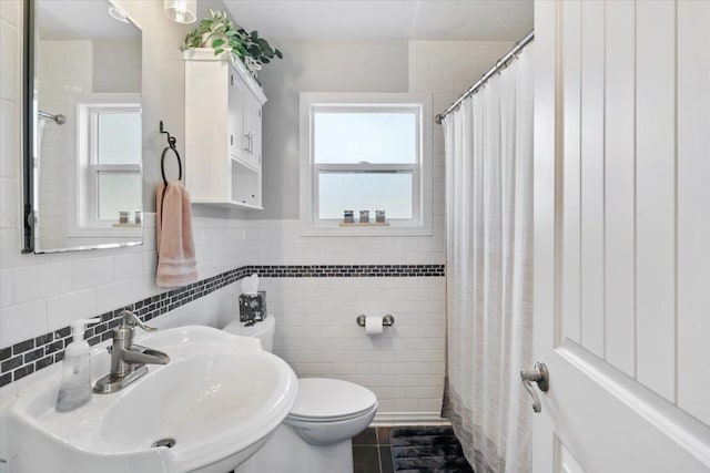 bathroom with toilet, tile walls, plenty of natural light, and a sink