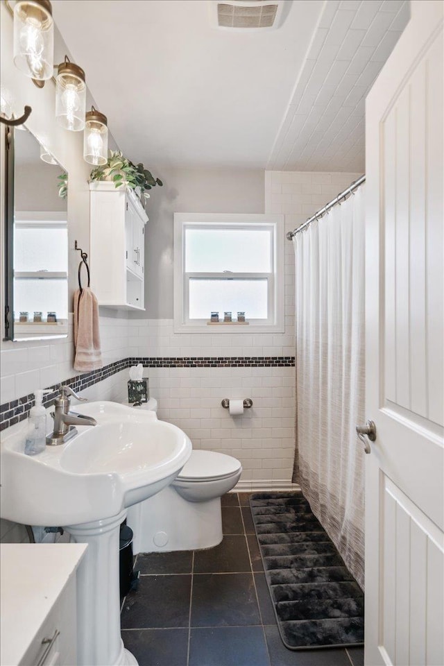 bathroom with visible vents, toilet, a shower with shower curtain, tile patterned floors, and tile walls