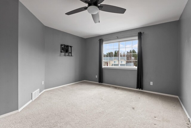 carpeted spare room with visible vents, baseboards, and a ceiling fan