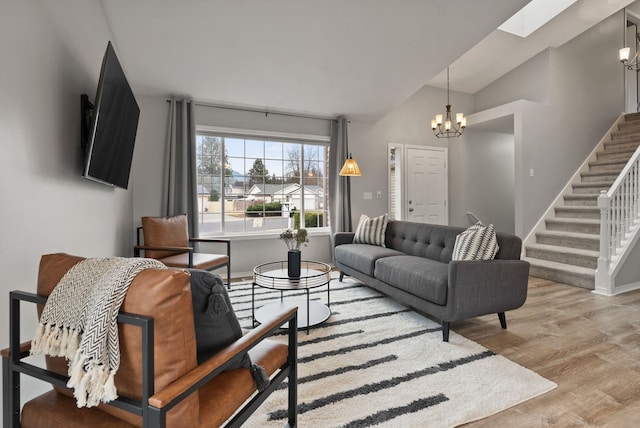 living area with stairway, wood finished floors, baseboards, lofted ceiling with skylight, and a notable chandelier