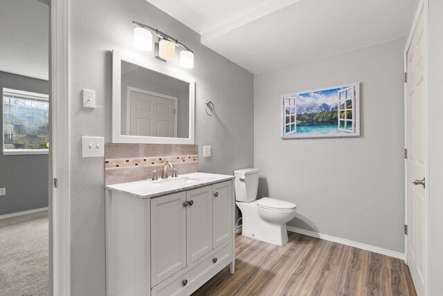 half bathroom featuring vanity, toilet, wood finished floors, and baseboards