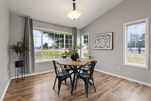 dining space with lofted ceiling, wood finished floors, baseboards, and visible vents