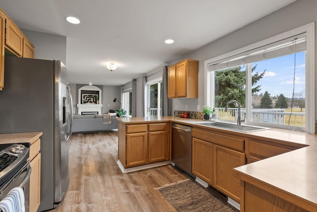 kitchen featuring a fireplace, a peninsula, light wood-style floors, stainless steel appliances, and a sink