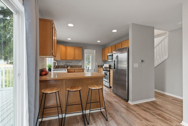 kitchen featuring light wood finished floors, a healthy amount of sunlight, appliances with stainless steel finishes, and a peninsula