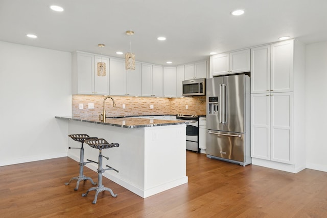 kitchen with a sink, light stone counters, wood finished floors, appliances with stainless steel finishes, and a peninsula