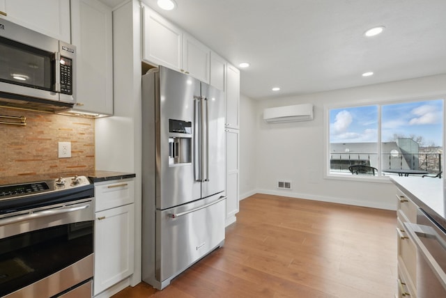 kitchen with visible vents, white cabinetry, a wall unit AC, stainless steel appliances, and decorative backsplash