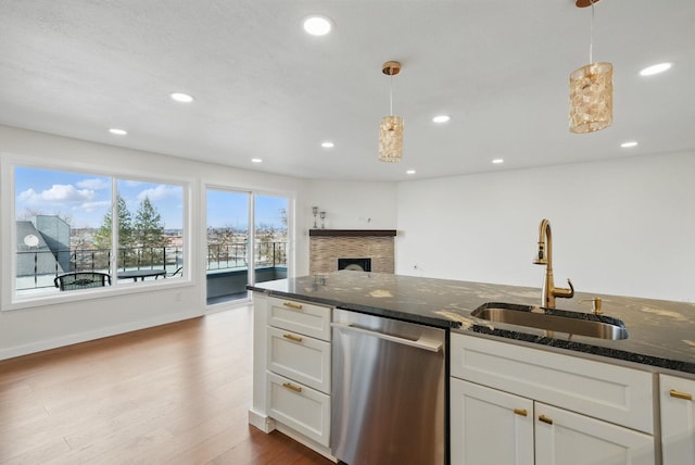 kitchen featuring dark stone counters, dark wood-style flooring, a fireplace, stainless steel dishwasher, and a sink