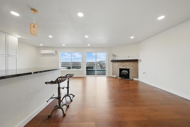 living room featuring a fireplace with raised hearth, baseboards, a wall mounted air conditioner, recessed lighting, and dark wood-style floors