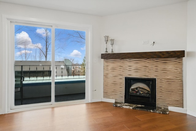 unfurnished living room featuring a fireplace with raised hearth, baseboards, and wood finished floors