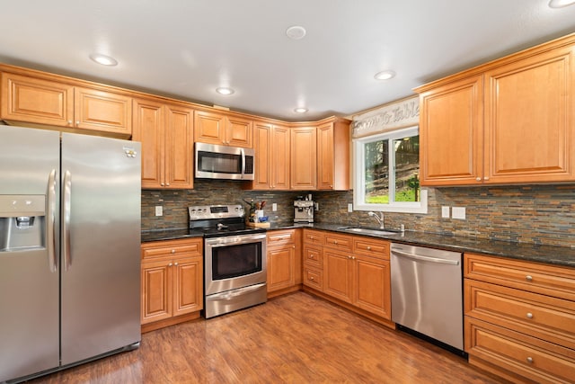 kitchen featuring light wood-style flooring, a sink, tasteful backsplash, stainless steel appliances, and dark stone counters