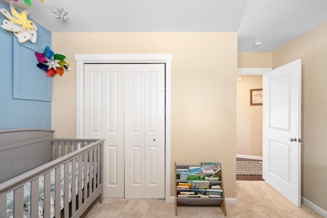 carpeted bedroom with a closet, a crib, and baseboards