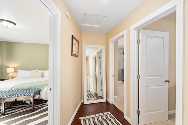 hall featuring baseboards, attic access, and dark wood finished floors