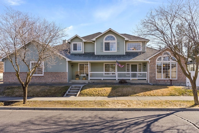 traditional-style house with a porch, brick siding, and a shingled roof