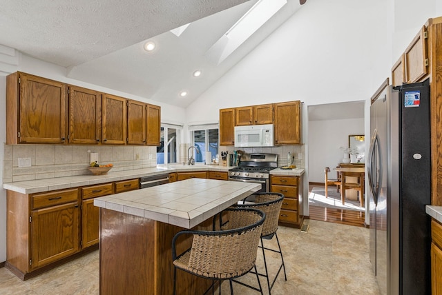 kitchen featuring a kitchen island, a skylight, a sink, stainless steel appliances, and a kitchen bar