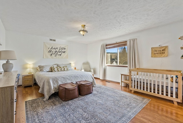 bedroom with wood finished floors, visible vents, and a textured ceiling