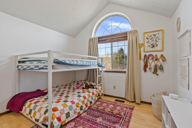 bedroom with light wood finished floors, visible vents, baseboards, vaulted ceiling, and a textured ceiling