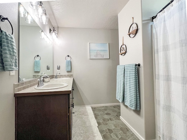 full bath with a textured ceiling, double vanity, baseboards, and a sink