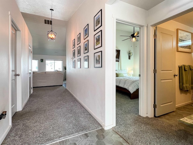 corridor with visible vents, carpet floors, a textured ceiling, and baseboards