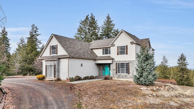 traditional-style house with stone siding, roof with shingles, and driveway