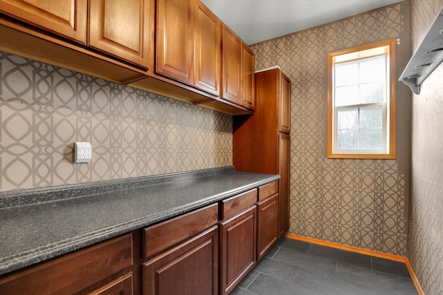 kitchen featuring dark countertops, dark tile patterned floors, wallpapered walls, and baseboards