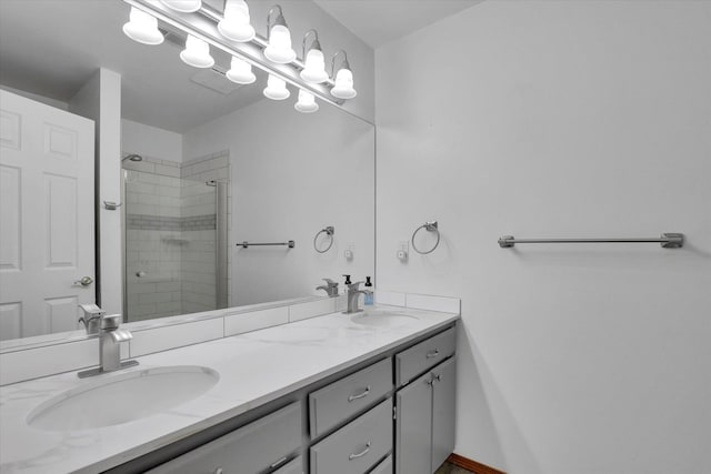 bathroom with double vanity, tiled shower, baseboards, and a sink