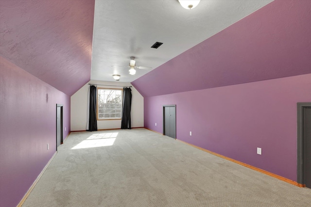 additional living space featuring visible vents, baseboards, vaulted ceiling, a textured ceiling, and light carpet