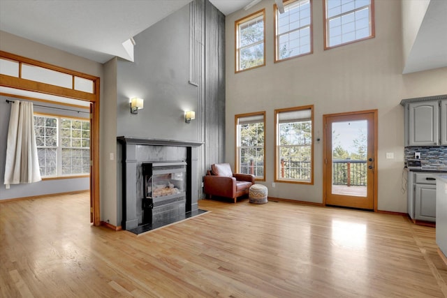 living room featuring a towering ceiling, baseboards, light wood finished floors, and a tile fireplace