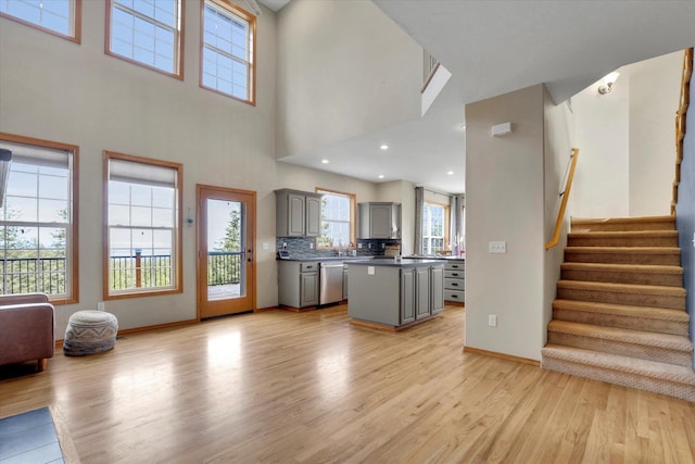 unfurnished living room featuring stairway, baseboards, a healthy amount of sunlight, and light wood-style flooring