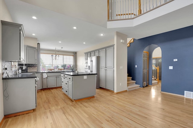 kitchen featuring a kitchen island, light wood-style flooring, arched walkways, gray cabinets, and dark countertops