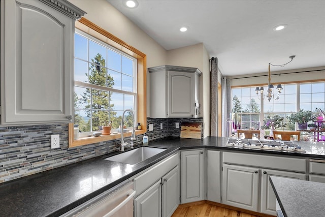 kitchen with a sink, tasteful backsplash, dark countertops, appliances with stainless steel finishes, and a chandelier