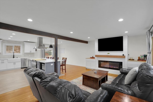 living area with a glass covered fireplace, beamed ceiling, recessed lighting, and light wood-style floors